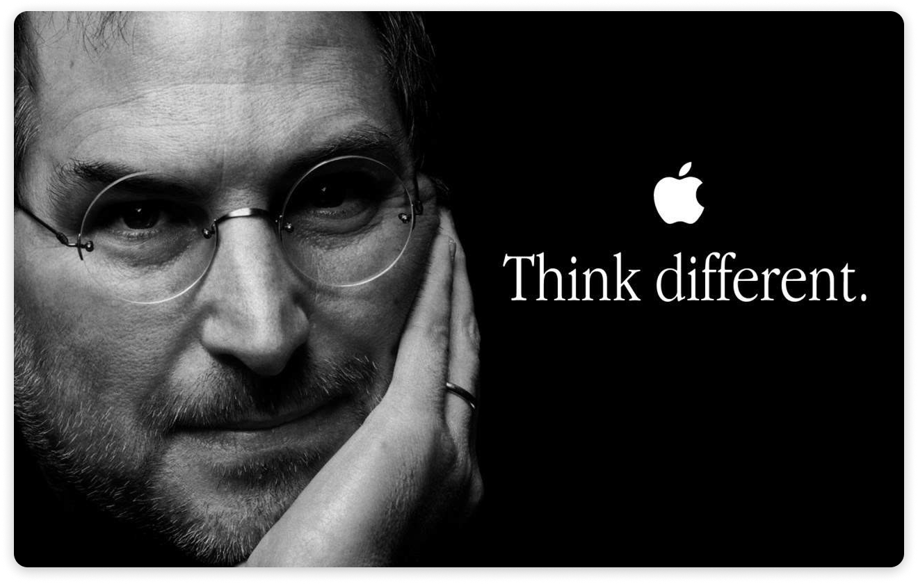 Black-and-white close-up portrait of a man wearing round glasses, with the Apple logo and the words ‘Think different.’ on a dark background.