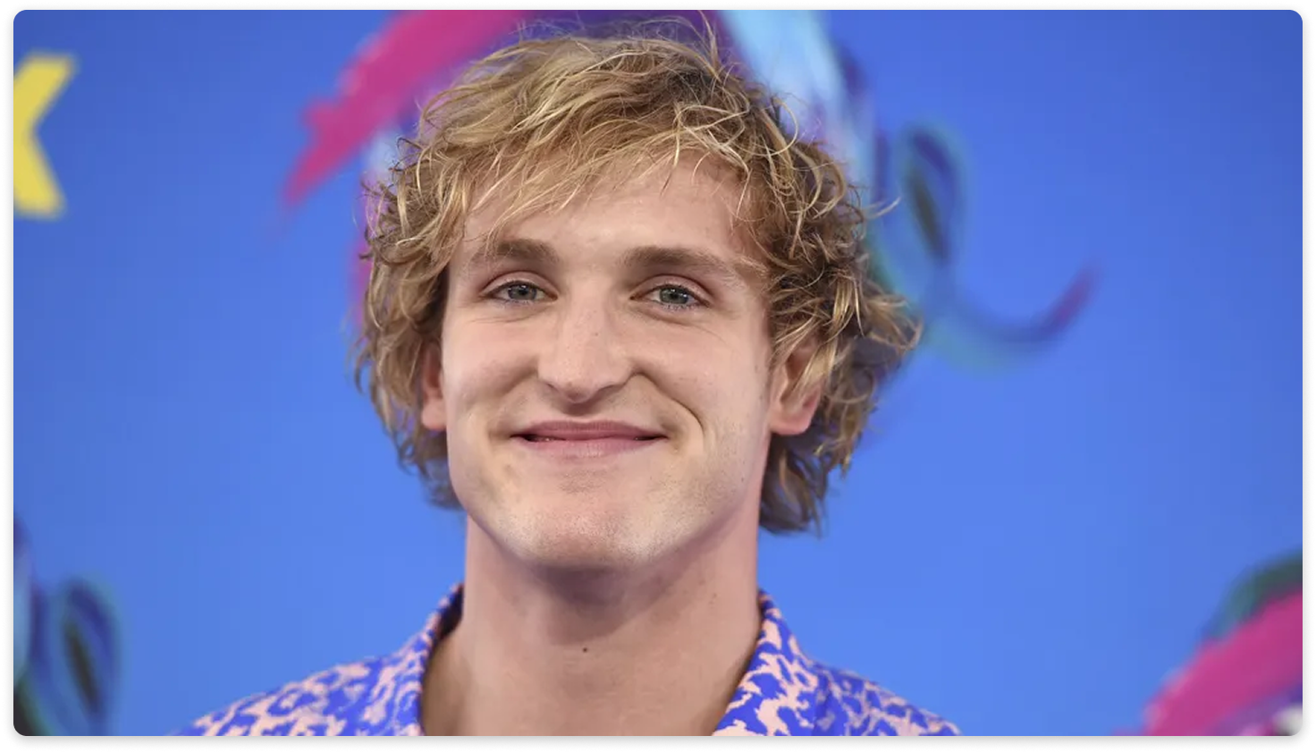 Smiling blond man in a patterned shirt against a blue backdrop.